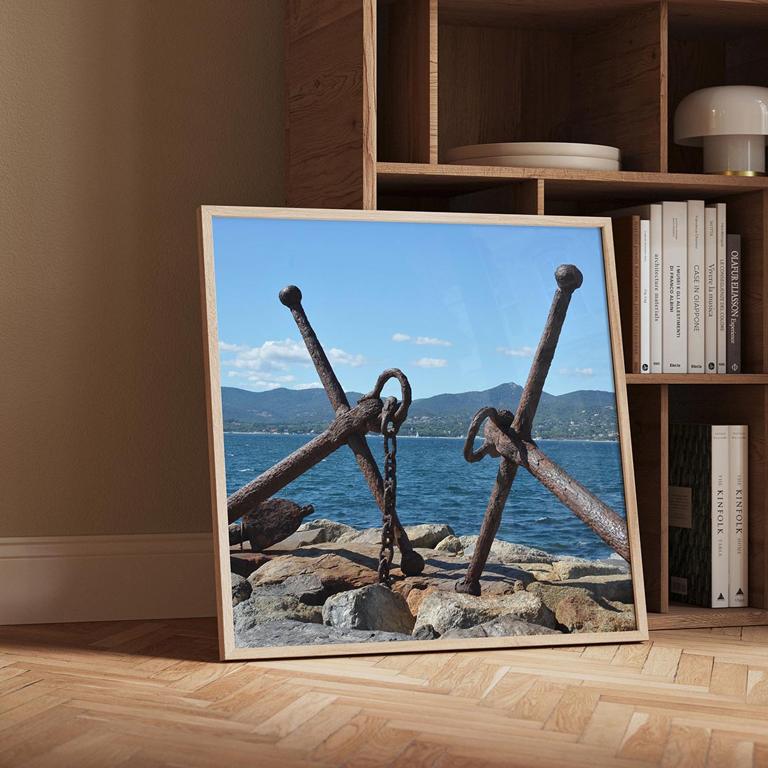 Ankers aan zee poster – detailweergave – twee verweerde ankers liggen op rotsen aan de kust, met een helderblauwe lucht en