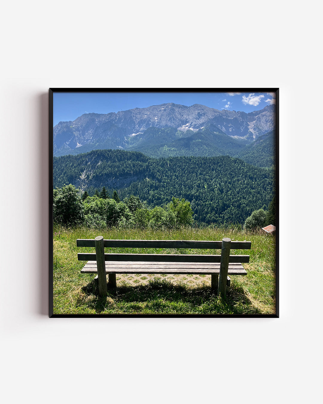 Berglandschap poster – vierkante wanddecoratie – een houten bankje staat op een groene heuvel met uitzicht op een bos en