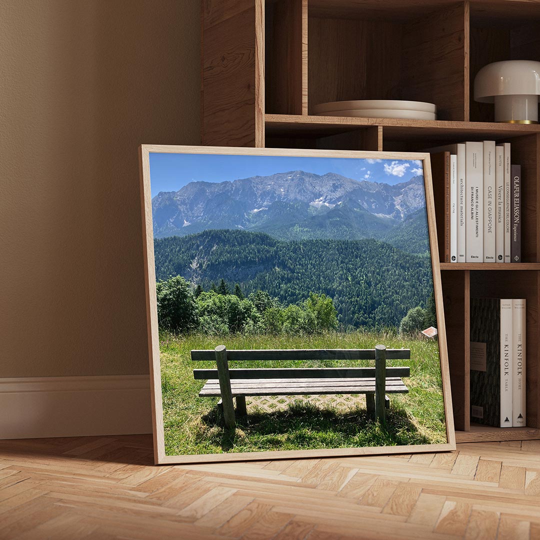 Berglandschap poster – detailweergave – een houten bankje staat op een groene heuvel met uitzicht op een bos en bergen onder
