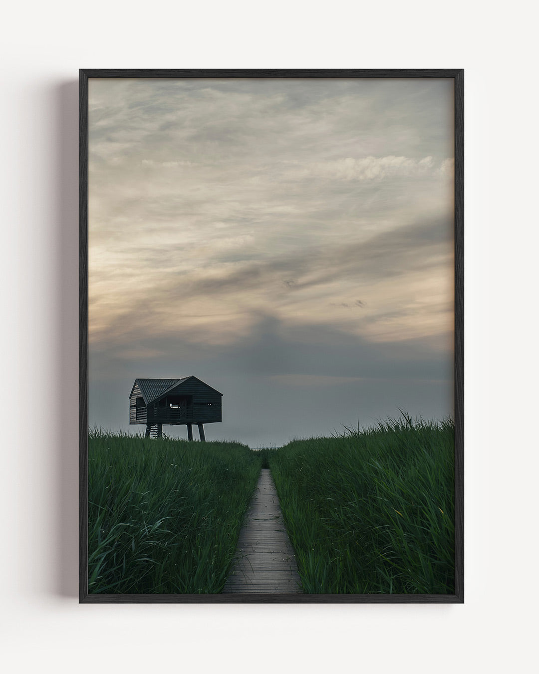 Houten huisje in gras poster – portret wanddecoratie – een houten huisje op palen staat in een weids graslandschap. De lucht